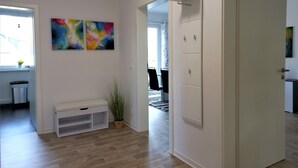 Una sala de estar moderna con suelo de madera, un banco blanco, una planta en maceta y arte abstracto en la pared.