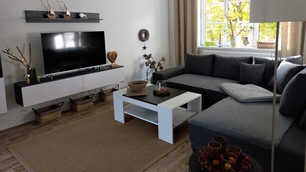 Una sala moderna con un televisor de pantalla plana, un sofá, una mesa de centro y un ventanal con vistas a árboles.