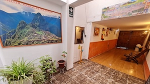 Eine Hotelhalle mit einem großen Poster von Machu Picchu, Fliesenboden, Topfpflanzen, einer Holztür und einem an der Wand befestigten Schild.