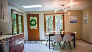 Une cuisine moderne avec un coin repas, comprenant une porte en bois ornée d’une guirlande, une table à manger avec des chaises et un lustre.