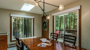 Une salle à manger spacieuse, dotée d’une grande table en bois, de nombreuses chaises et offrant une vue sur une forêt grâce à de grandes fenêtres.