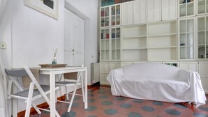 Ein Zimmer mit einem weißen Tisch und Stühlen, einer gepolsterten Couch, einem Bücherregal und einem sechseckig gefliesten Boden.