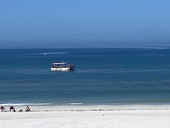 A beach with a boat in the water and a few people on the shore.