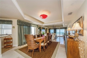 A spacious dining area with a wooden table and wicker chairs, a ceiling fan, and a view of the ocean.