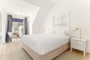 Relax in this cozy retreat with a large bed, nightstand, and chair, surrounded by natural light and a view of lush greenery.