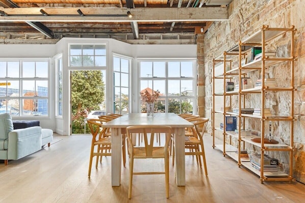 Enjoy meals in this dining area with a long table and six chairs, surrounded by large windows offering a view of the outdoors.