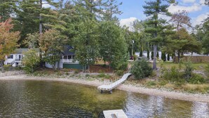 A lakeside property with a dock, a house, and surrounding trees. - Lakeside Living w\sandy beach, gas fireplace -easy 25 minute commute to Portland (Gray)