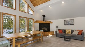 A spacious living room with a wooden dining table, benches, a sofa, and a fireplace. - Lakeside Living w\sandy beach, gas fireplace -easy 25 minute commute to Portland (Gray)