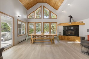 Un salón amplio con techo alto, ventanas grandes, chimenea y zona de comedor.