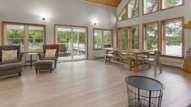 A spacious living area with a wooden ceiling, large windows, a dining table, and comfortable seating. - Lakeside Living w\sandy beach, gas fireplace -easy 25 minute commute to Portland (Gray)