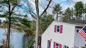 A white house with pink shutters, a dock, and a flag.