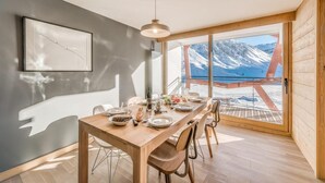 A dining area with a wooden table set for four, a pendant light, and a view of snow-covered mountains through large windows. - 200m from ski slopes, 5th floor, view mountain, balcony, ski locker, 100m², Tignes (Tignes)
