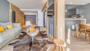 A modern living room with a sofa, coffee table, and a rug. There is a kitchen area with a dining table and chairs. - 200m from ski slopes, 5th floor, view mountain, balcony, ski locker, 100m², Tignes (Tignes)