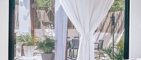 A bedroom with a large bed, a view of an outdoor patio with chairs and plants, and a wooden pergola.