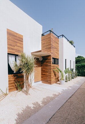A modern building with a mix of white and wooden panels, a concrete pathway, and potted plants.
