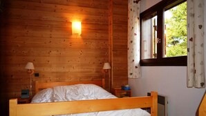 Et træhus-værelse med seng, to sengeborde med lamper, et vindue med gardiner og en fastgjort varmeovn.
