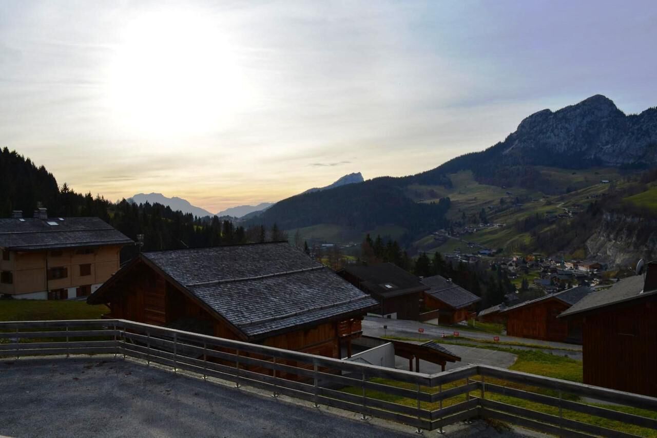A mountain village with traditional wooden houses, a small building with a sloped roof, and a view of the surrounding hills and mountains.