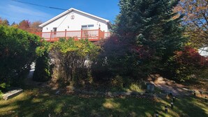 Une maison blanche avec un porche rouge et un grand arbre à feuilles persistantes devant.