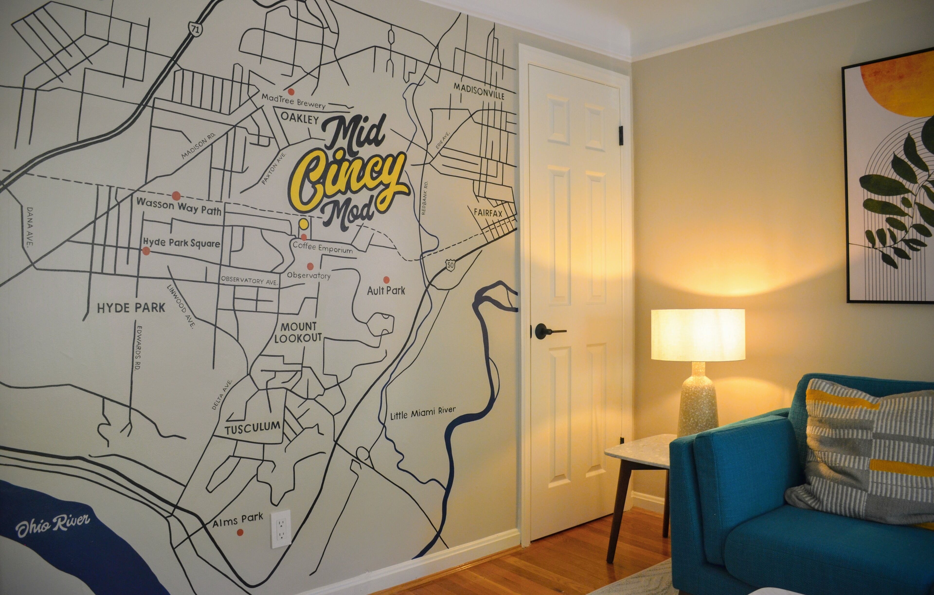 Een kaart van Midden-Cincinnati op een muur, een deur, een lamp en een blauwe bank.