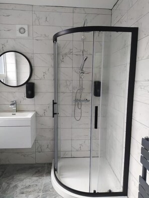 Een moderne badkamer met een douchecabine van glas, een witte wastafel en een wand betegeld met marmer.
