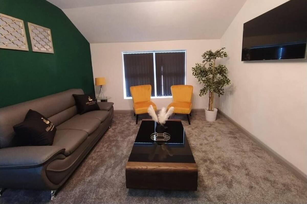 A living room with a sofa, two armchairs, a coffee table, a TV, and a window with curtains.