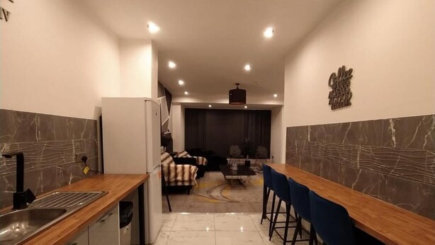A modern kitchen with a marble backsplash, a wooden countertop, and a built-in refrigerator. There is a seating area with a sofa and a coffee table in the background. - Black Pearl Luxury Apartments (Blackpool)