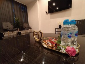 Een vergaderruimte met een glanzende tafel, een hartvormige decoratie, een dienblad met snacks, waterflessen en een roos.