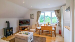 A cozy living room with a fireplace, a TV, a dining table with chairs, and a window with curtains. - Idyllic Retreat in The Cotswolds (Chipping Campden)