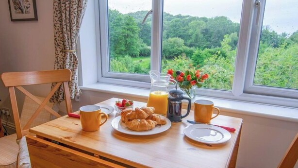 A breakfast table with croissants, a pitcher of orange juice, and a mug, set by a window with a view of greenery. - Idyllic Retreat in The Cotswolds (Chipping Campden)