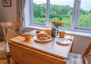 Una mesa de desayuno con cruasanes, una jarra de jugo de naranja y una taza, junto a una ventana con vistas a follaje.