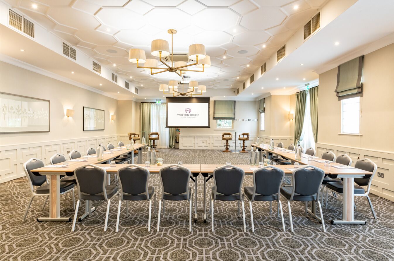 A conference room with a long table, chairs, a projector screen, and a modern chandelier.
