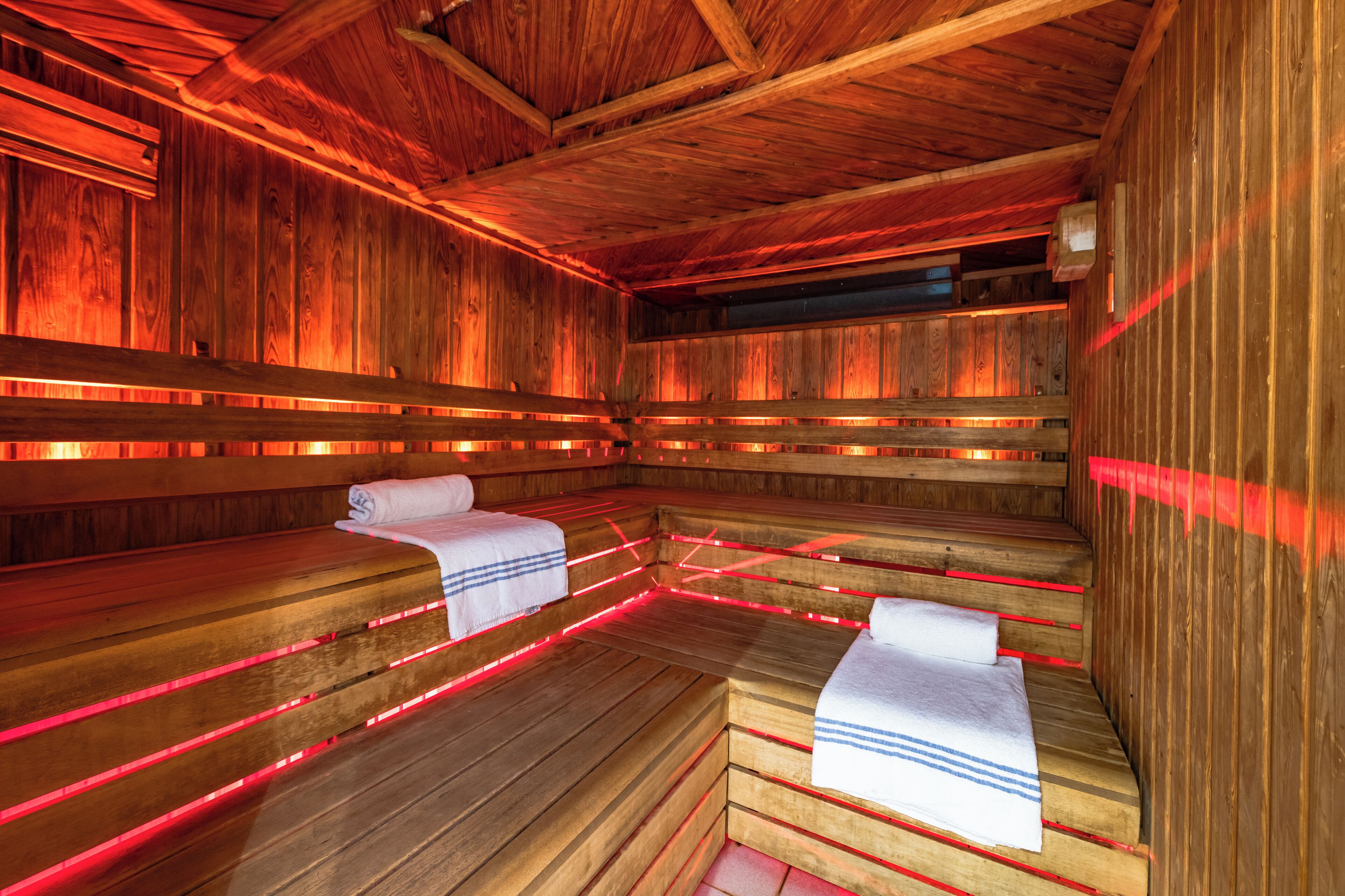 A sauna with wooden benches and red lighting.