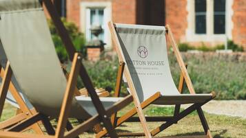 Dos sillones de lona con la marca 'WOTTON HOUSE COUNTRY ESTATE HOTEL', ubicados sobre césped frente a un edificio de ladrillo.