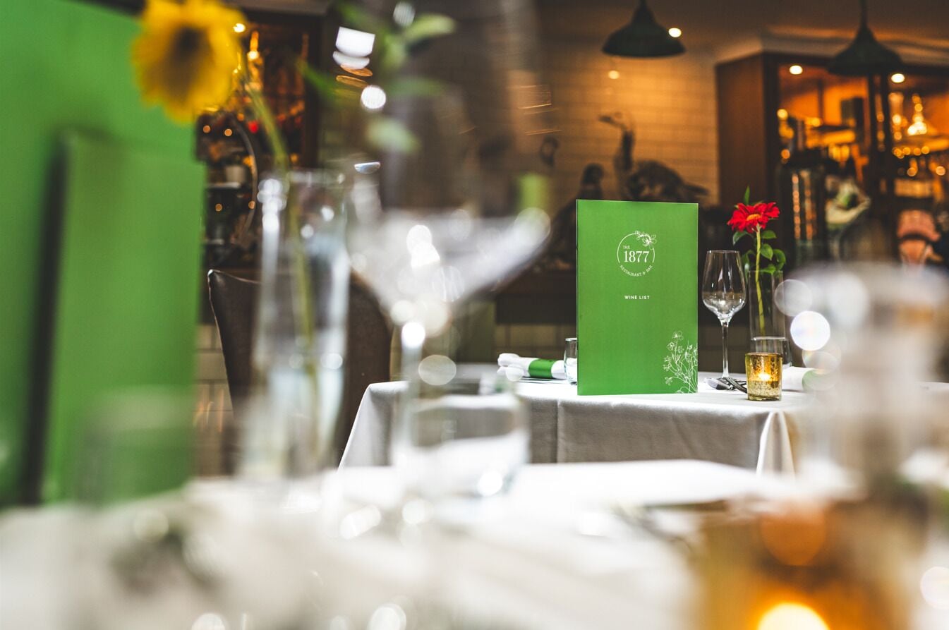 A restaurant setting with a green menu stand, a vase with a sunflower, and a wine glass on the table.