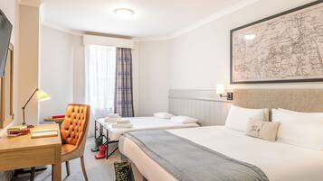 A hotel room with two beds, a desk with a lamp, a chair, and a map on the wall.