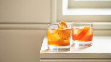 Two glasses of amber-colored beverage with ice and orange slices on a wooden surface.