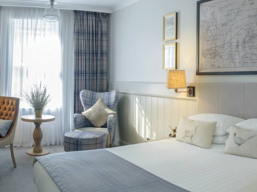 A hotel room with a bed, a desk with a chair, a small table with a plant, and a map on the wall.