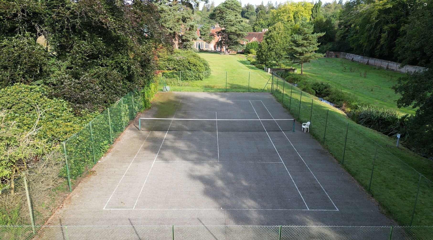 En tenniskort omgiven av frodig grönska och en traditionell byggnad i bakgrunden.