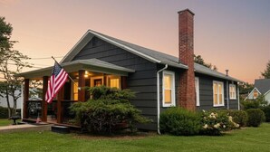 Een twee verdiepingen tellend huis met een bakstenen schoorsteen, een veranda met een Amerikaanse vlag en een verzorgd gazon.
