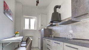 A modern kitchen with grey cabinets, a stainless steel range hood, and a window providing natural light. - Voyager House Apartment (Roma)