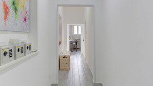 A narrow hallway with a white door at the end, a small table with a chair, and a colorful abstract painting on the wall. - Voyager House Apartment (Roma)