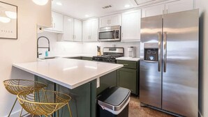 Een moderne keuken met witte kasten, roestvrijstalen apparatuur en een centraal keukenblok met zitplaatsen.