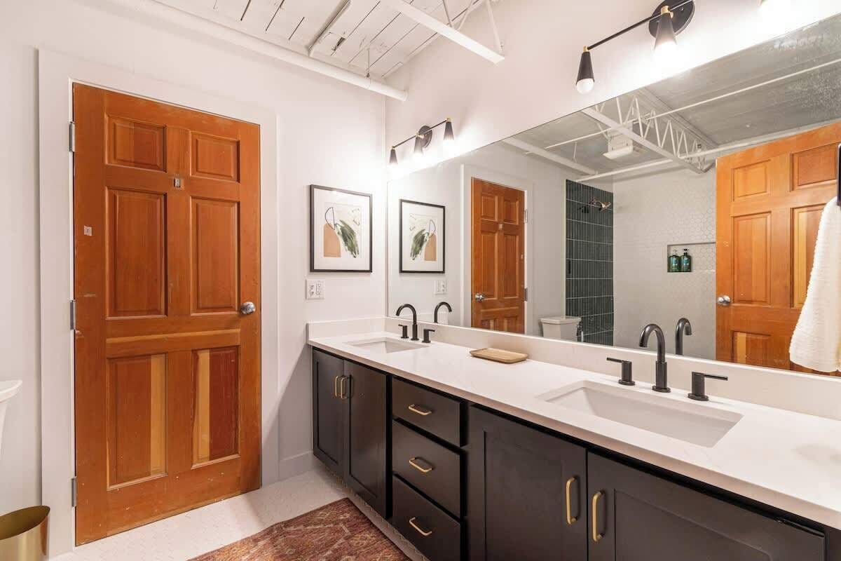 A modern bathroom with a large mirror, two sinks, dark cabinets, and wooden doors.