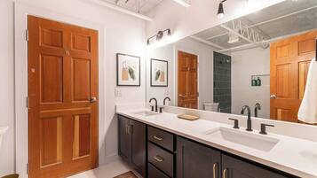 A modern bathroom with a large mirror, two sinks, dark cabinets, and wooden doors.