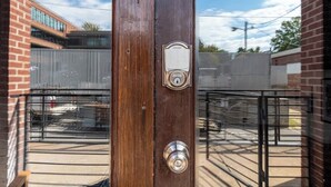 Een houten stutpaal met een metalen hangslot en een metalen plaatje, omringd door een metalen hek en een gebouw op de achtergrond.