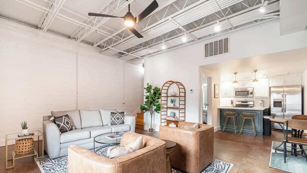Een ruime woonkamer met een bank, twee fauteuils, een salontafel en een keuken op de achtergrond.