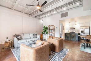 A spacious living area with a sofa, two armchairs, a coffee table, and a kitchen in the background.
