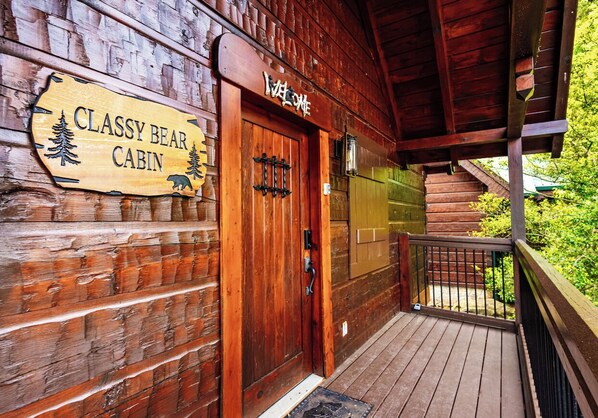 Uma cabana de madeira com uma placa que diz "CLASSY BEAR CABIN" e uma porta com puxador de metal.