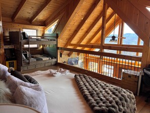 Quarto de cabana aconchegante com beliche, cama grande e vista para um deck de madeira pela janela.