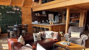 L’intérieur chaleureux d’un chalet comprend un coin repas en bois, un bar et un espace salon avec des canapés en cuir et une table basse.